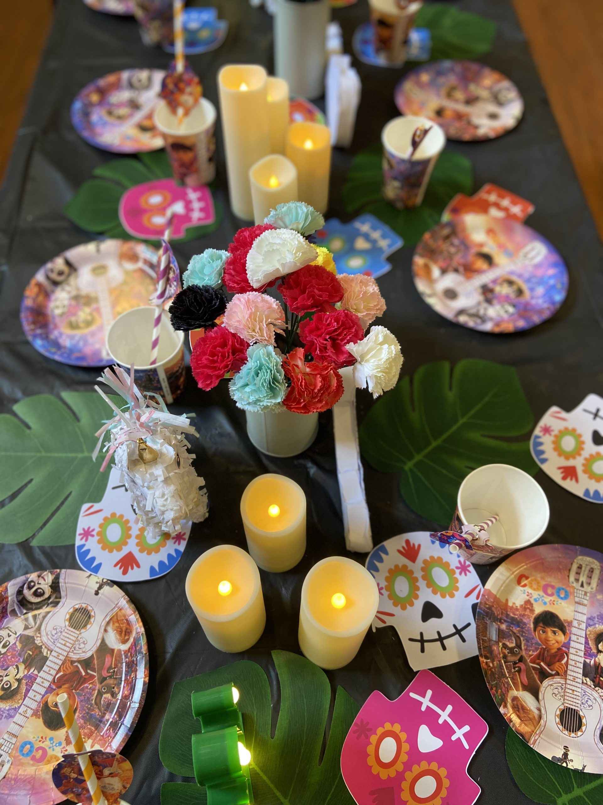 Coco themed kids' party tablescape with vibrant Marigold flowers, colorful papel picado banners, and a festive table setting featuring bright plates, themed cups, and elegant tableware for a luxurious celebration